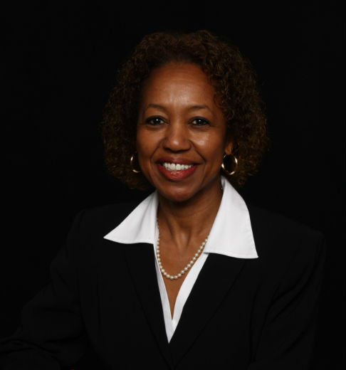Professional woman in black suit smiling against a dark background.